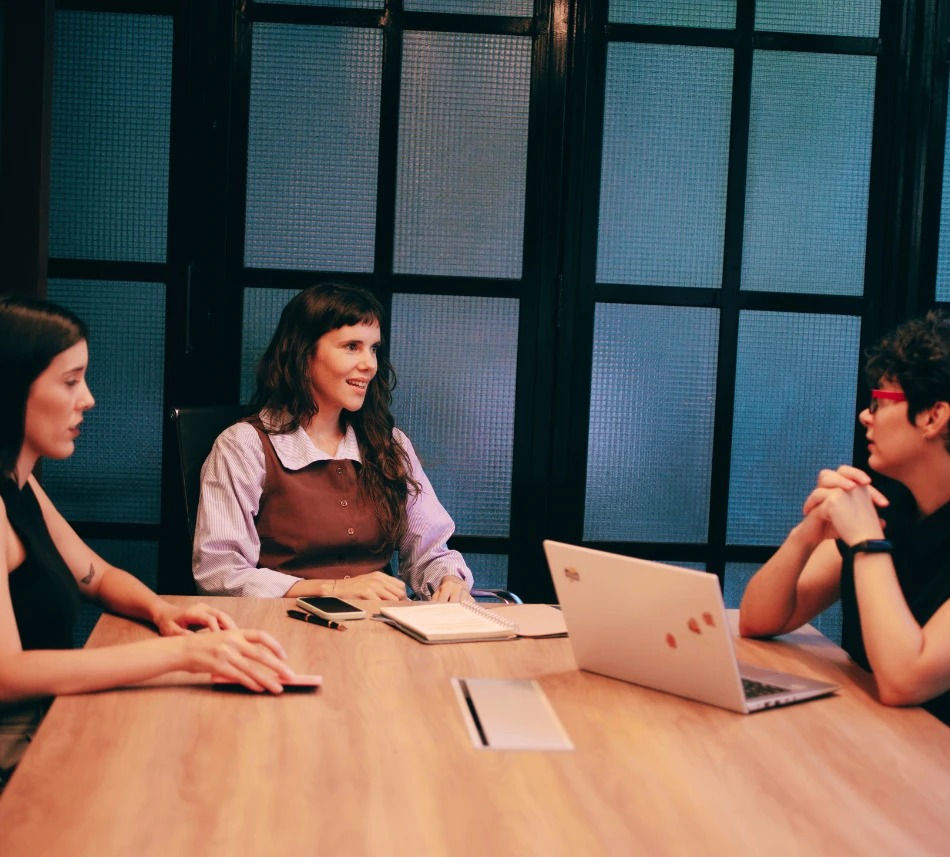 Una de las socias de Proyecto SHE explicando en una mesa de trabajo mientras las otras dos escuchan