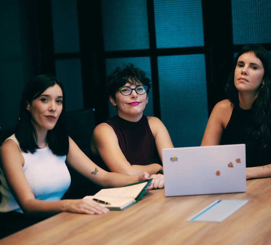 Las tres socias de Proyecto SHE sentadas juntas en una mesa de trabajo, con una notebook abierta